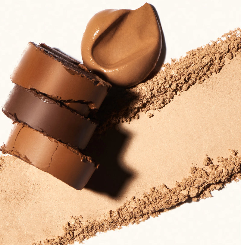 Pressed mineral powder closeup and top down shot of three powder and one liquid foundation in brown and tan tones against white background. 