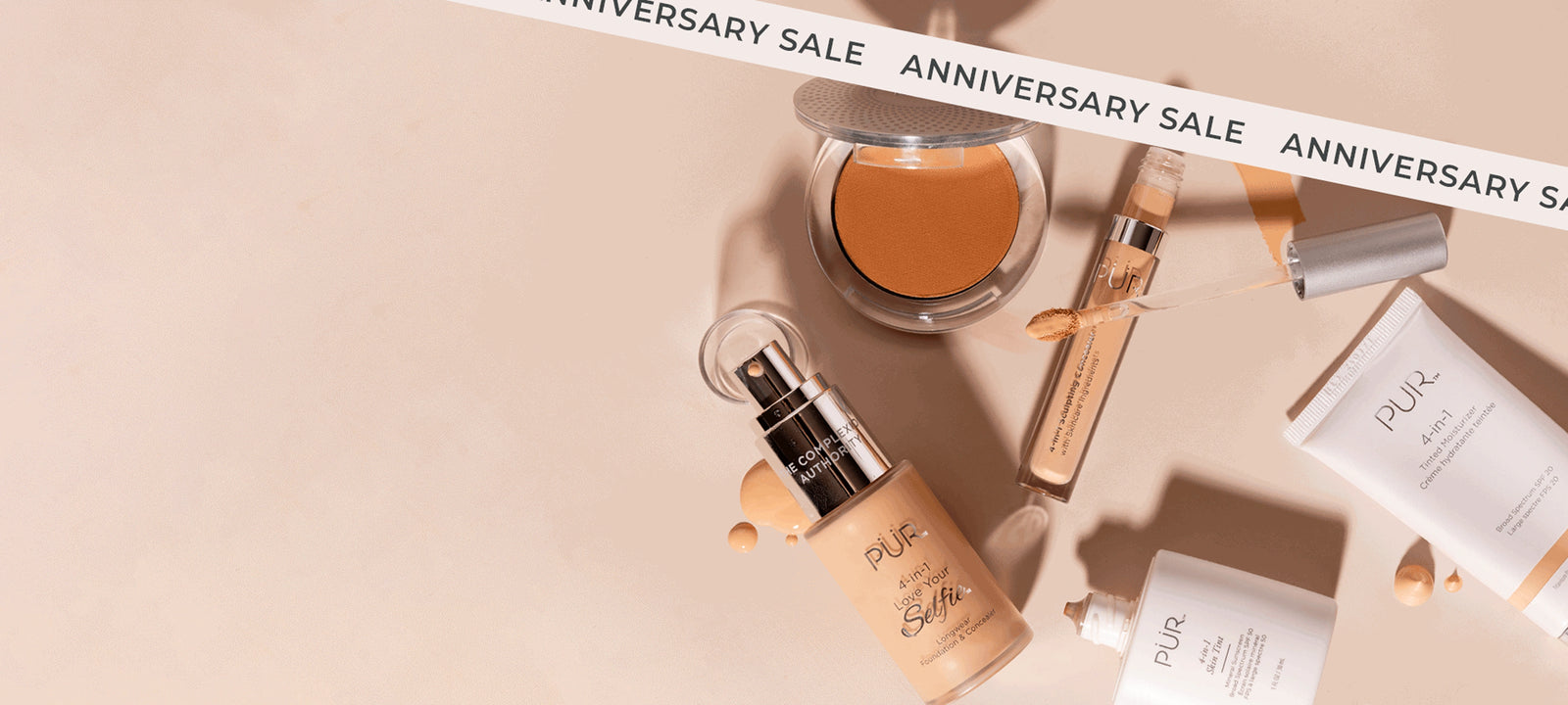 PÜR Anniversary Sale 2026 - 35% Off Sitewide: Various makeup bottles and containers laying against cream background with "Anniversary Sale" banner (desktop)