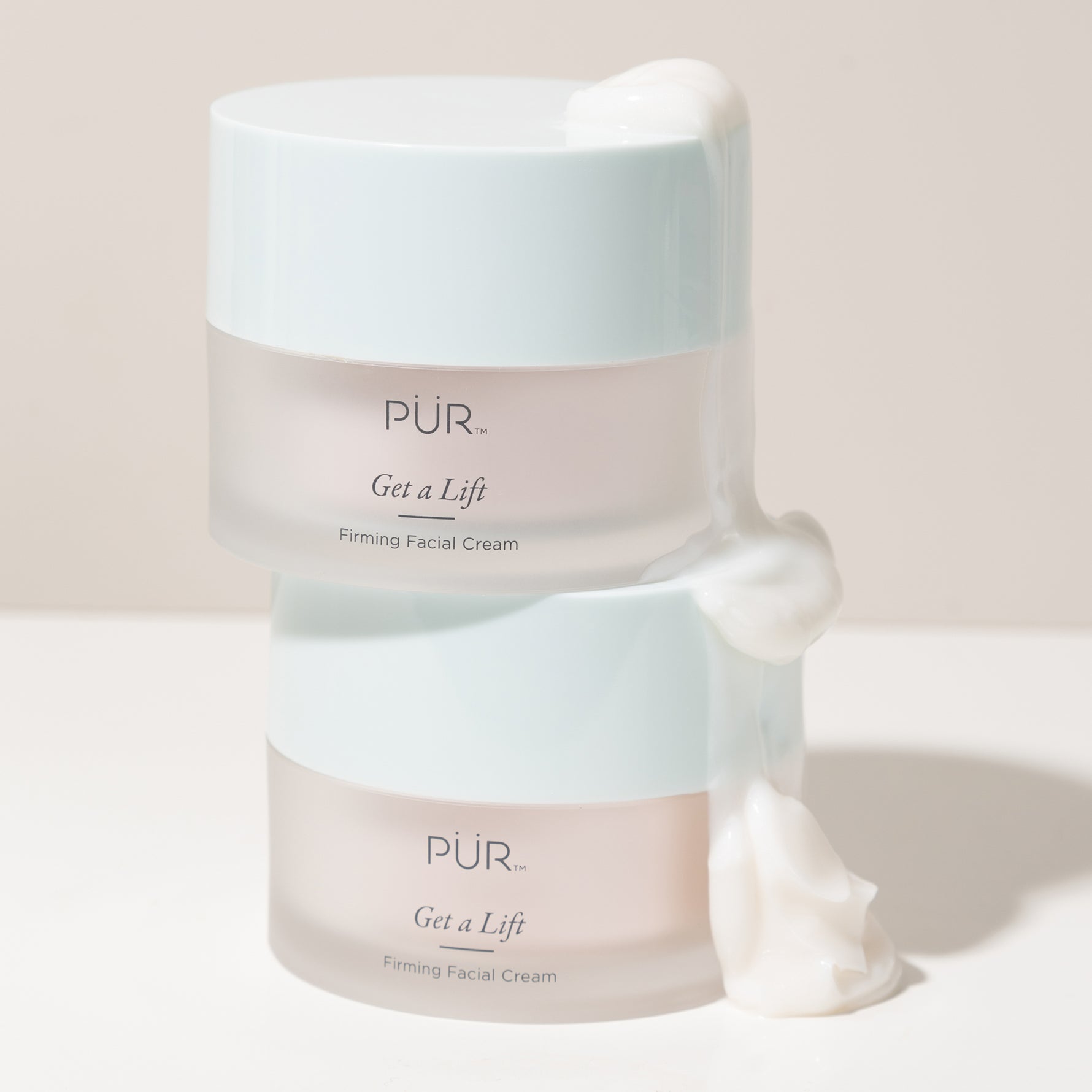 Two stacked jars of PÜR Get A Lift Firming Facial Cream with product spilling over the sides for a luxurious texture shot.